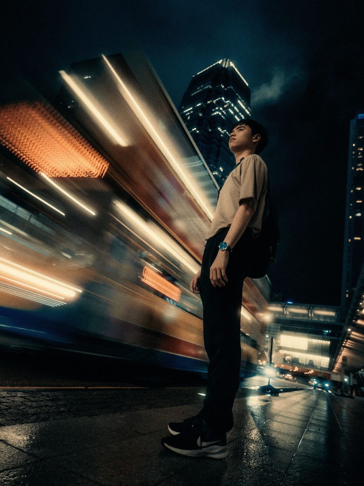 A man standing still on a night street while a tram rushes past as streaks of light