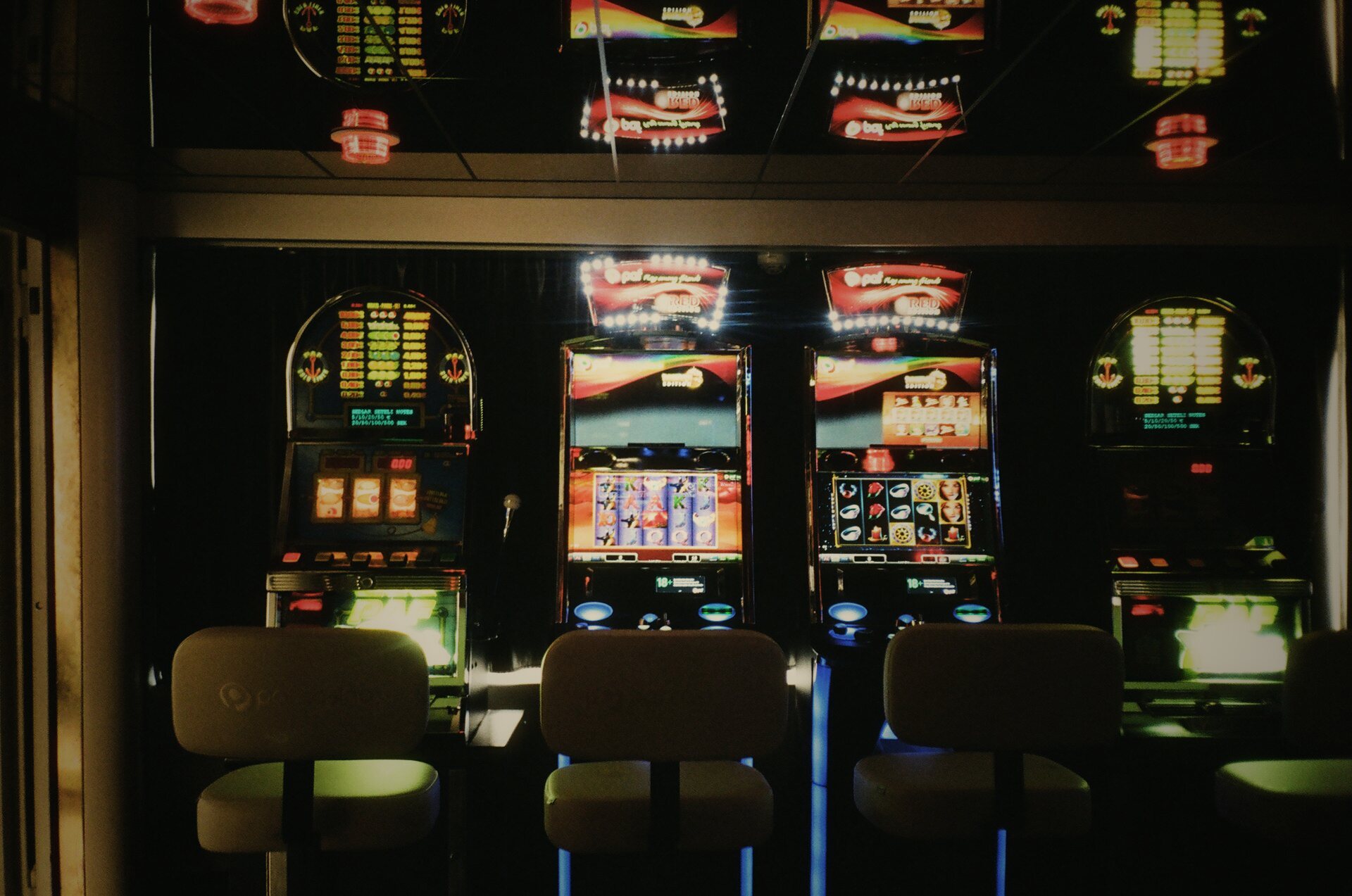 A dim room of slot machines, lit up and waiting, chairs empty